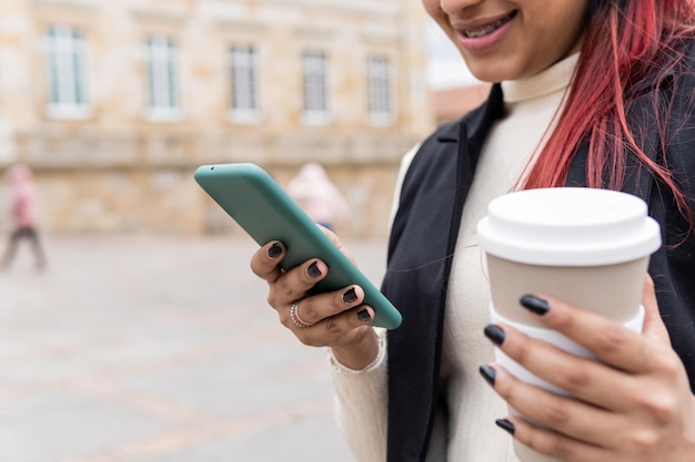 Uma mulher está olhando para o telefone enquanto segura uma xícara de café na praça da cidade