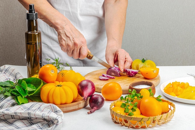 Uma mulher está preparando uma salada de tomate Legumes maduros ervas especiarias aromáticas azeite Cozinha caseira ingredientes frescos