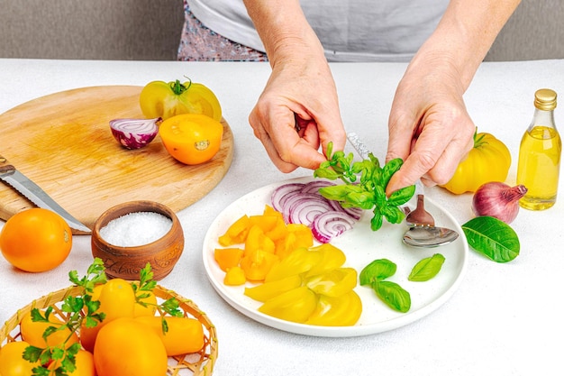 Uma mulher está preparando uma salada de tomate Legumes maduros ervas especiarias aromáticas azeite Cozinha caseira ingredientes frescos