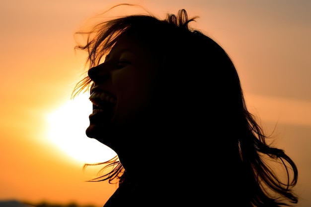 Uma mulher está rindo na frente de um pôr do sol.