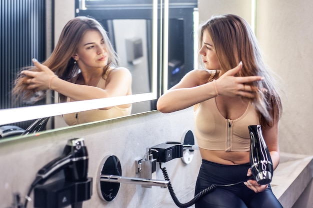 Uma mulher está se olhando no espelho e segurando um secador de cabelo.