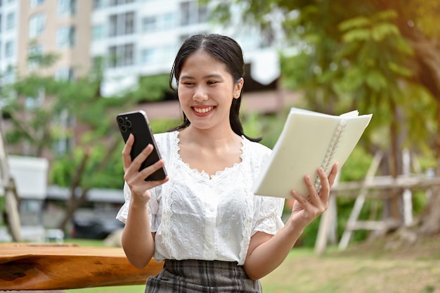 Uma mulher está segurando um livro e olhando para a tela do smartphone enquanto relaxa ao ar livre