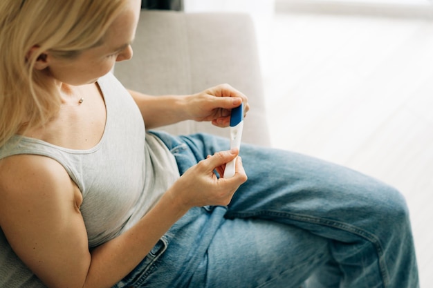 Foto uma mulher está segurando um teste de gravidez em suas mãos e esperando o resultado sentada no sofá