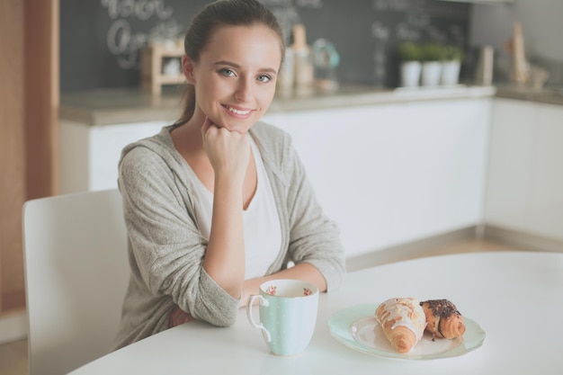 Uma mulher está sentada à mesa com um prato de comida e um croissant.