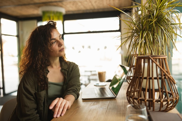 Uma mulher está sentada à mesa de um café, olhando para um laptop.