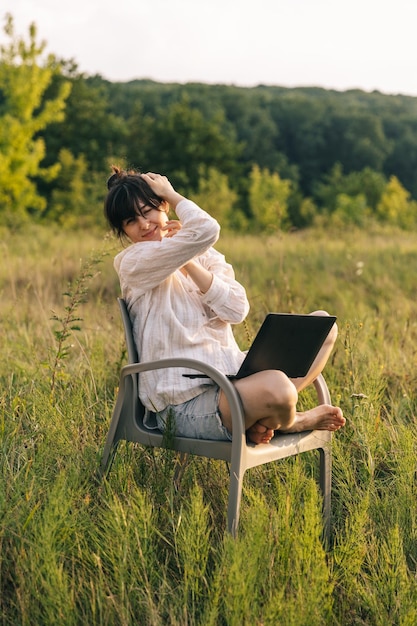 Uma mulher está sentada em uma cadeira em um campo com um laptop no colo.