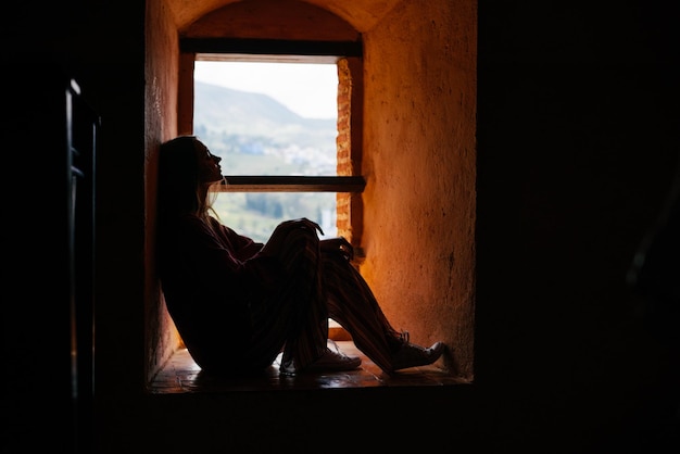 Foto uma mulher está sentada em uma janela com o sol brilhando através de seus olhos.