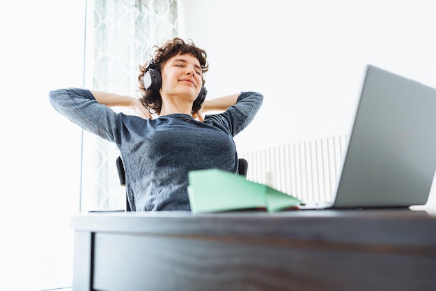 Uma mulher está sentada em uma mesa com fones de ouvido e um laptop na frente dela.