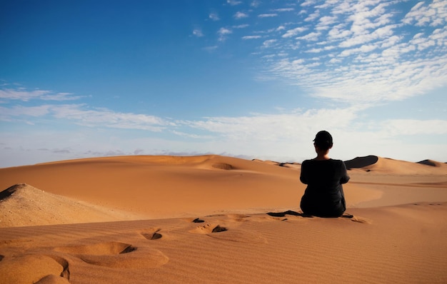 Uma mulher está sentada na duna de areia dourada do deserto do namibe. áfrica