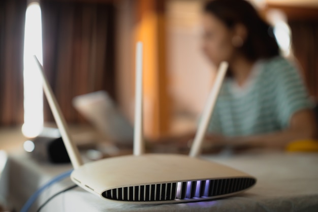 Uma mulher está trabalhando em casa usando um roteador de modem, conectando a internet ao seu laptop.