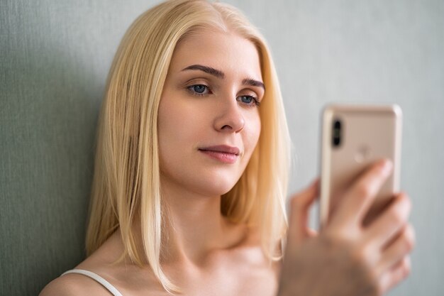 Uma mulher está usando seu smartphone enquanto sorri deitada na cama.