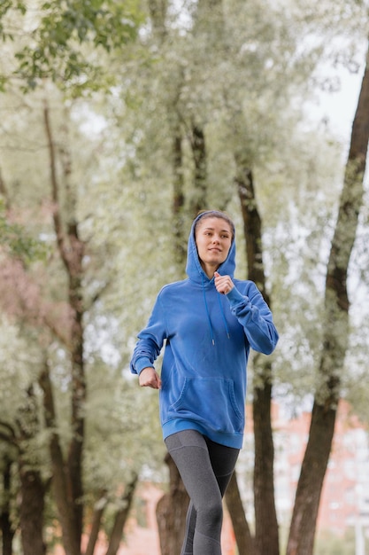 Uma mulher europeia com um capuz azul está correndo e praticando esportes no parque fitness e ioga ao ar livre