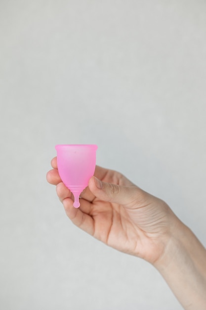 Uma mulher europeia segura nas mãos um copo menstrual rosa feito de silicone para higiene e cuidados femininos