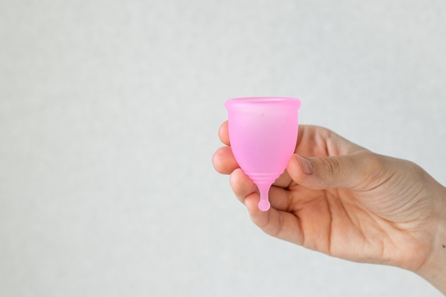 Uma mulher europeia segura nas mãos um copo menstrual rosa feito de silicone