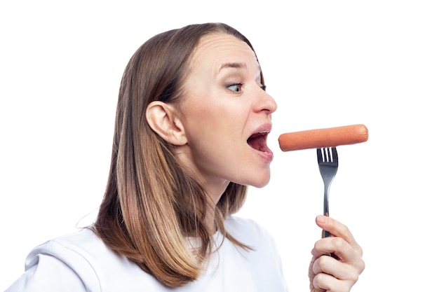 Uma mulher faminta com a boca aberta come uma salsicha de um garfo Deliciosa comida rápida Isolada no fundo branco Detalhe