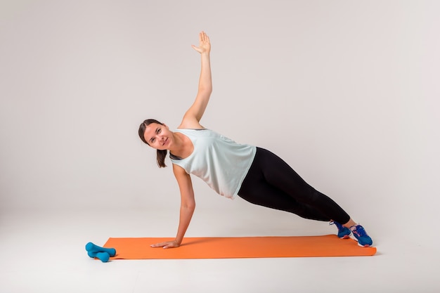 Uma mulher faz uma prancha lateral e olha para a câmera em um branco com espaço para texto