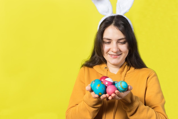 Foto uma mulher feliz com orelhas de coelho na cabeça segura ovos de páscoa e sorrisos