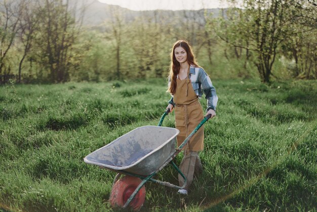 Uma mulher feliz com um carrinho trabalha em sua casa de campo no campo contra um pano de fundo de grama verde e sol do pôr do sol