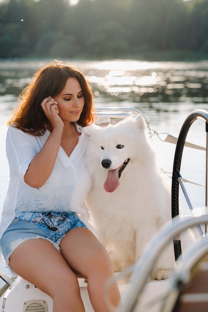 Uma mulher feliz com um grande cachorro branco em um iate branco no mar