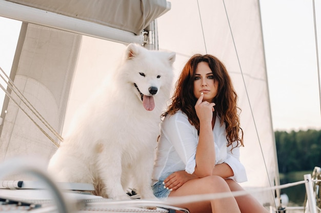 Uma mulher feliz com um grande cachorro branco em um iate branco no mar.