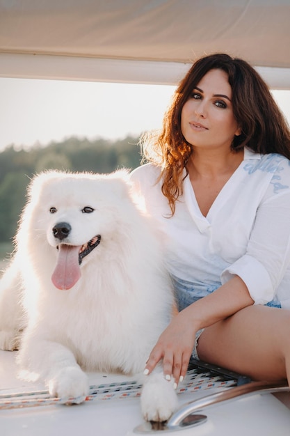 Uma mulher feliz com um grande cachorro branco em um iate branco no mar.