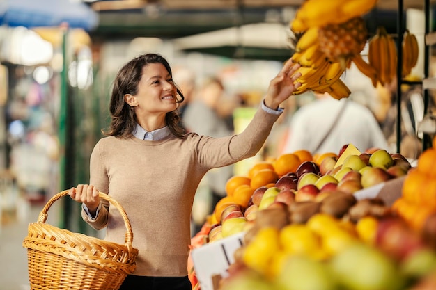 Uma mulher feliz com uma cesta nas mãos escolhendo frutas orgânicas no mercado dos agricultores