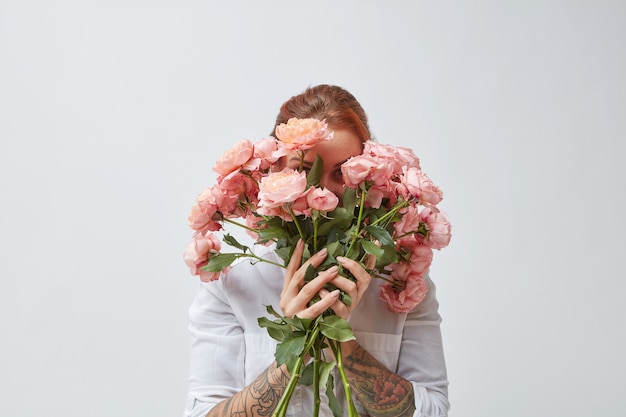 Uma mulher feliz com uma tatuagem nas mãos esconde o rosto atrás de um buquê de rosas perfumadas. Dia das Mães