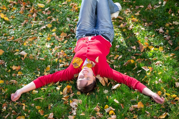 Uma mulher feliz de meia-idade está deitada na grama com folhas de outono