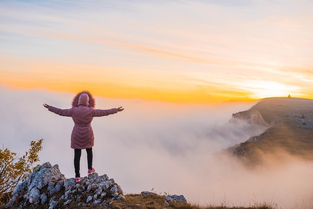 Uma mulher feliz e livre de braços abertos desfruta de uma pausa no topo da montanha ao pôr do sol