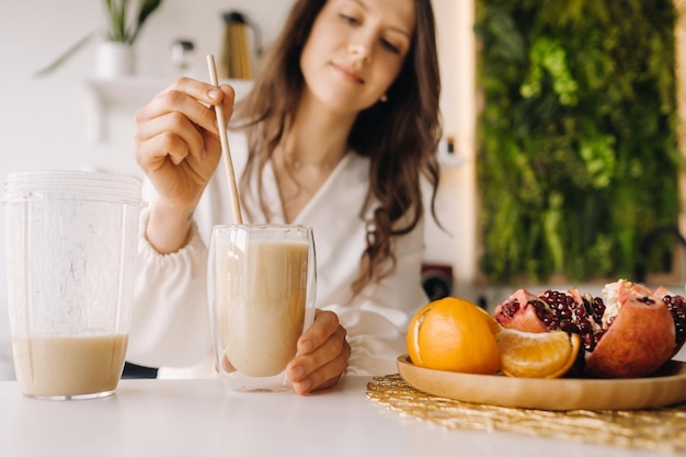 Uma mulher feliz e saudável fez um coquetel de frutas em pé na cozinha em casaComida saudável