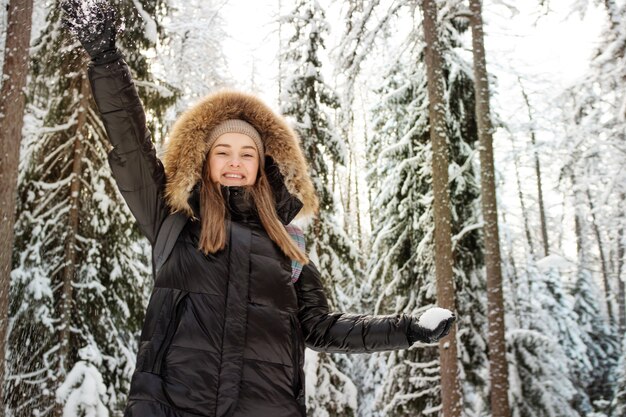 Uma mulher feliz e sorridente com um capuz de pele na cabeça joga neve em você