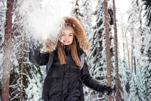 Uma mulher feliz e sorridente com um capuz de pele na cabeça joga neve em você