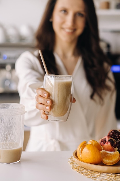 Uma mulher feliz e sorridente e saudável preparou um coquetel de frutas e dá a você enquanto está em casa na cozinhacomida saudável