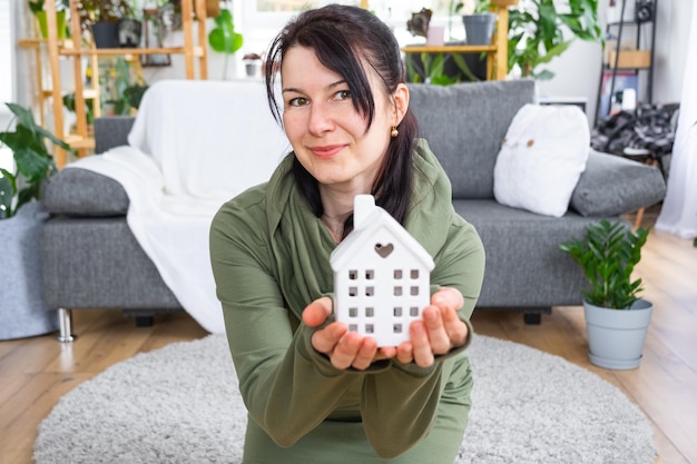 Uma mulher feliz em sua casa tem nas mãos uma figura em miniatura de uma casa e uma chave no interior Projeto de casa de sonho compra de imóveis seguro hipoteca aluguel reserva