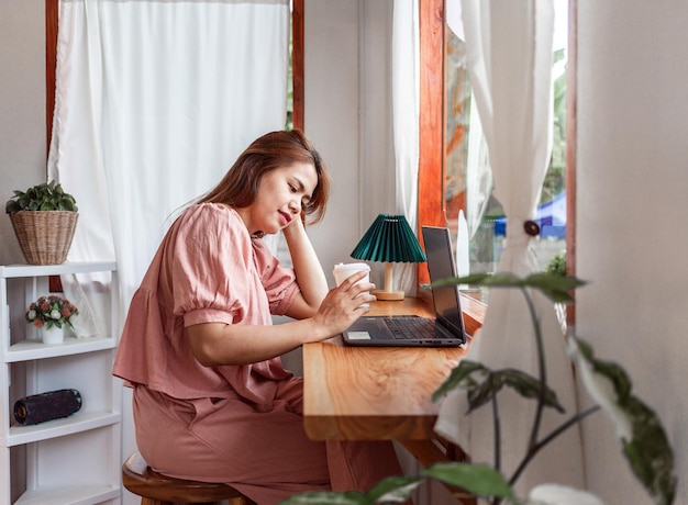 Uma mulher feliz em um café usando um laptop na mão e uma xícara de café de papel