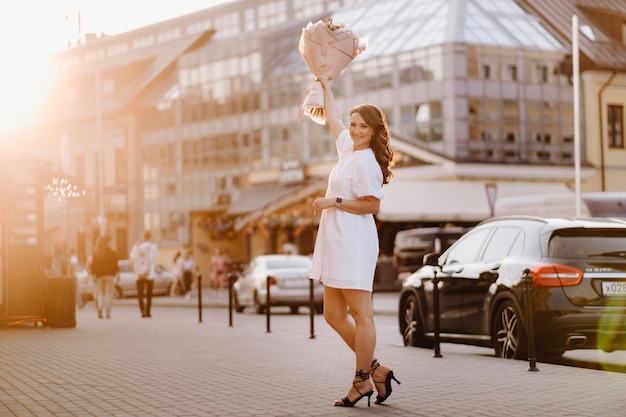 Uma mulher feliz em um vestido branco ao pôr do sol com um buquê de flores na cidade