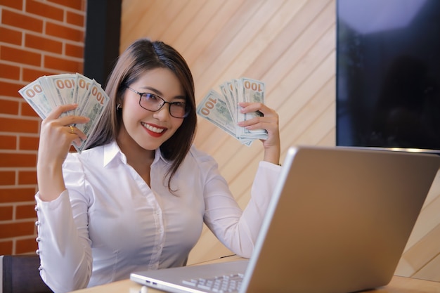 Foto uma mulher feliz está carregando dólares enquanto estiver usando um laptop. ela conseguiu investir.