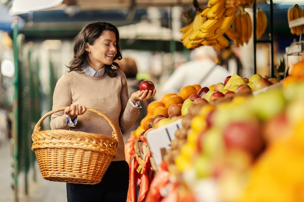 Uma mulher feliz está escolhendo frutas orgânicas no mercado