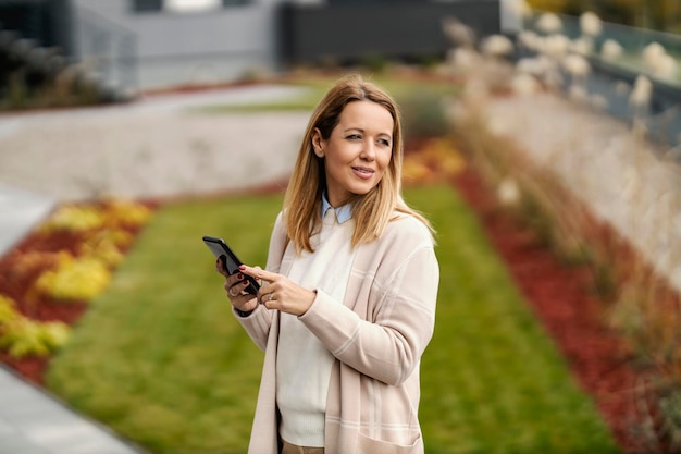 Uma mulher feliz está parada na rua e usando o telefone para mensagens online