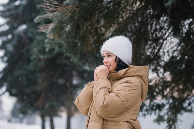 Uma mulher feliz fica de casaco e aquece as mãos Fica na cidade no inverno sob a neve