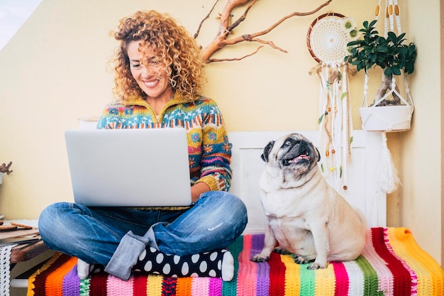 Uma mulher feliz usando laptop ao ar livre em casa sentada perto de seu melhor amigo cão pug e desfrutando de tecnologia e amizade Trabalho feminino alegre e atraente no computador em conexão sem fio Lazer