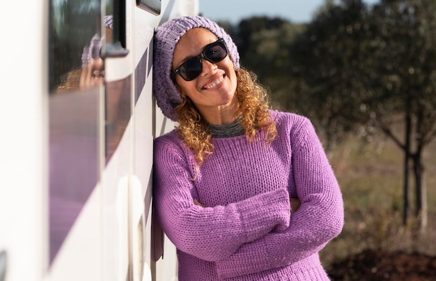 Uma mulher feliz viajante em pé e posando sorrindo para a câmera contra sua van moderna branca motorhome pequena casa Conceito alternativo de viagem e liberdade Pessoas femininas aventuram sozinhas