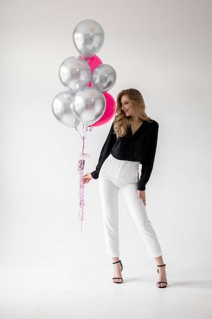 Uma mulher fica ao lado de um balão rosa que diz 'aniversário' nele