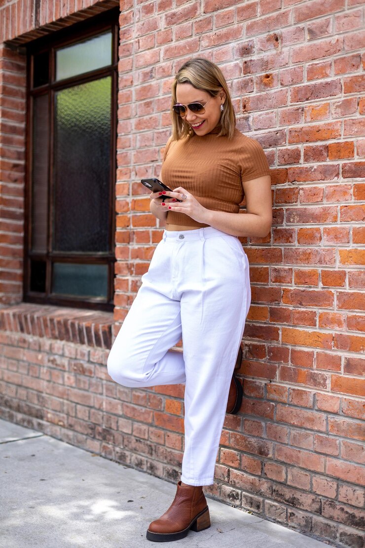 Foto uma mulher fica em frente a uma parede de tijolos e olha para o telefone