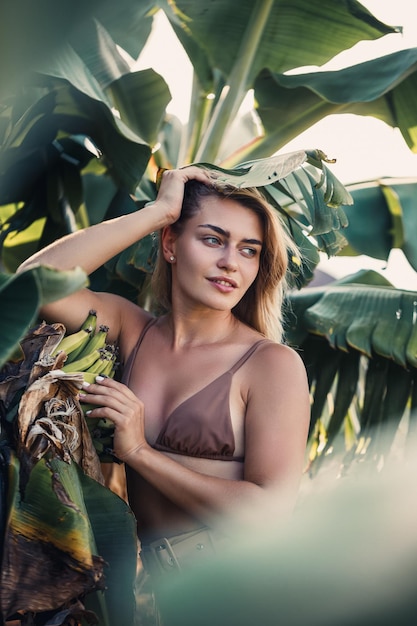 Uma mulher fica perto de folhas de banana verde na ilha Árvores tropicais