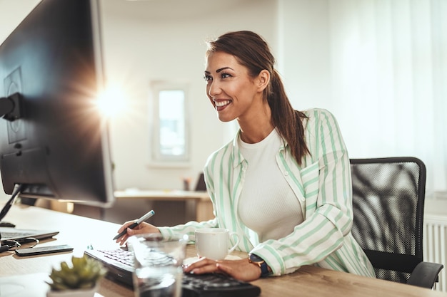 Uma mulher freelance sorridente bem-sucedida está trabalhando em um novo projeto no escritório. ela está olhando para o projeto em um computador.