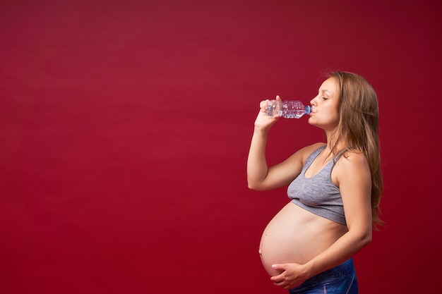 Uma mulher grávida bebe água. Com sede. Aprecia o sabor da água pura. Estilo de vida de gravidez. Copie o espaço.