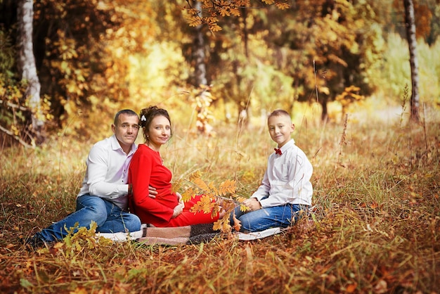 Uma mulher grávida com seu marido e filho em um parque de outono