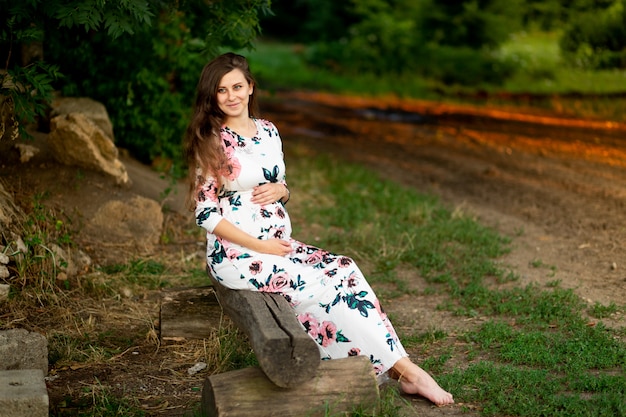 Uma mulher grávida com um vestido caminha na floresta no verão