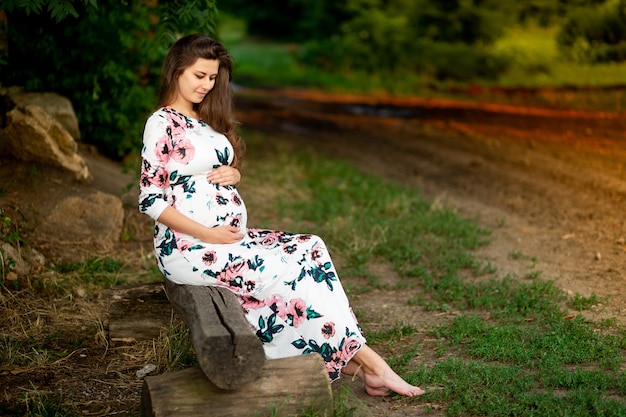 Uma mulher grávida com um vestido caminha na natureza na floresta no verão